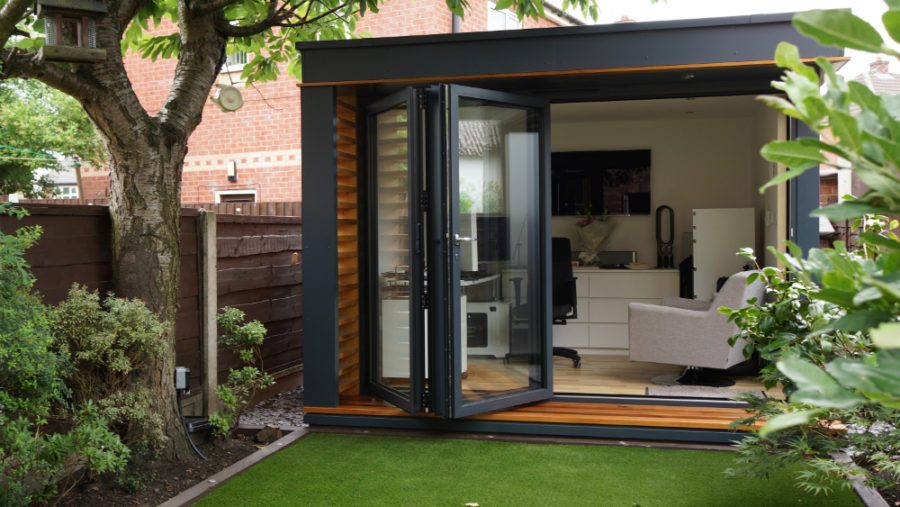 A detached backyard office with folding glass doors opening onto a lawn